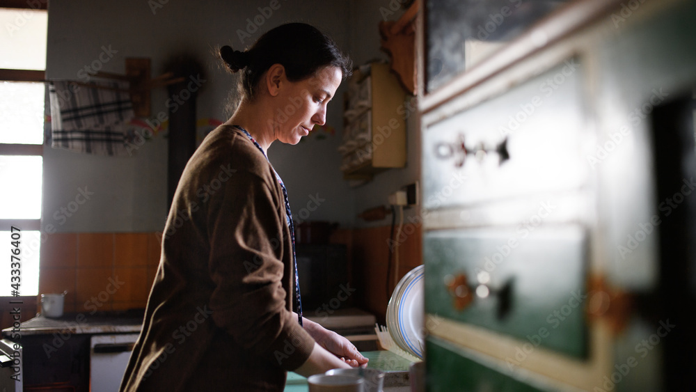 Poor mature woman washing dishes indoors at home, poverty concept. Poor mature woman washing dishes indoors at home, poverty concept.