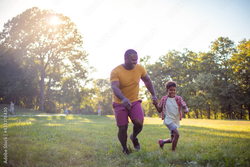 Fototapeta premium African American father and son in nature. Son and dad running together.