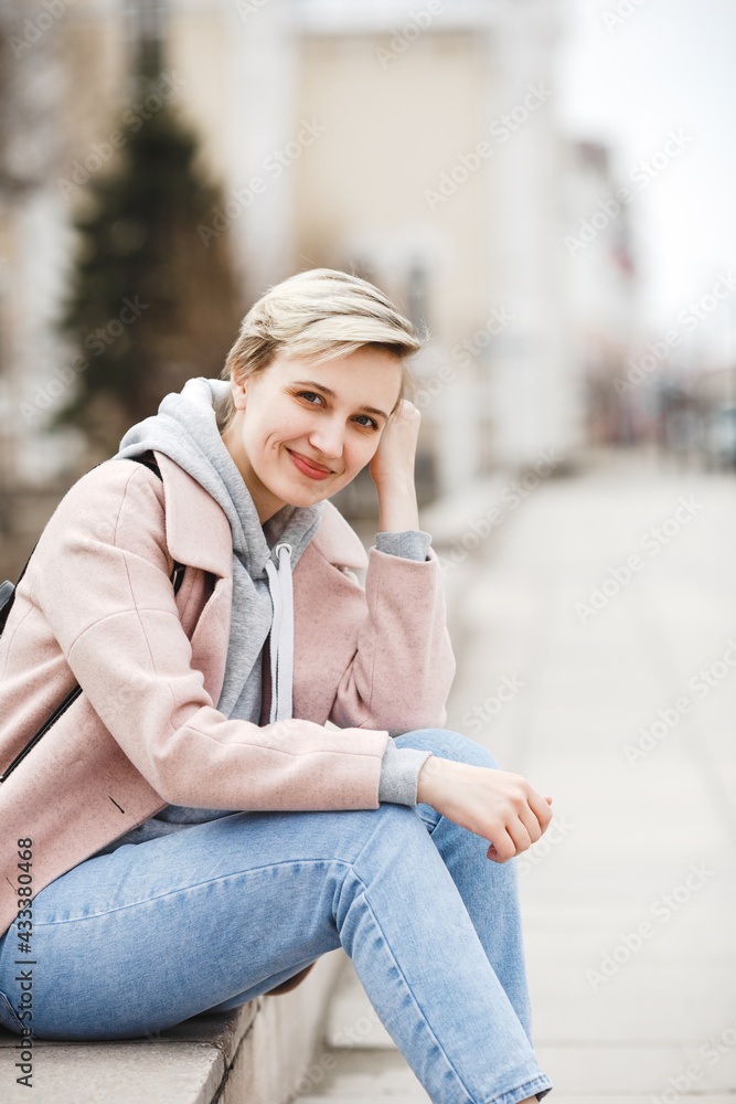 Attractive hipster blonde girl in a pink coat walks around beautiful authentic old town. The concept of freedom. creativity and inspiration Attractive hipster blonde girl in a pink coat walks around beautiful authentic old town. The concept of freedom. creativity and inspiration