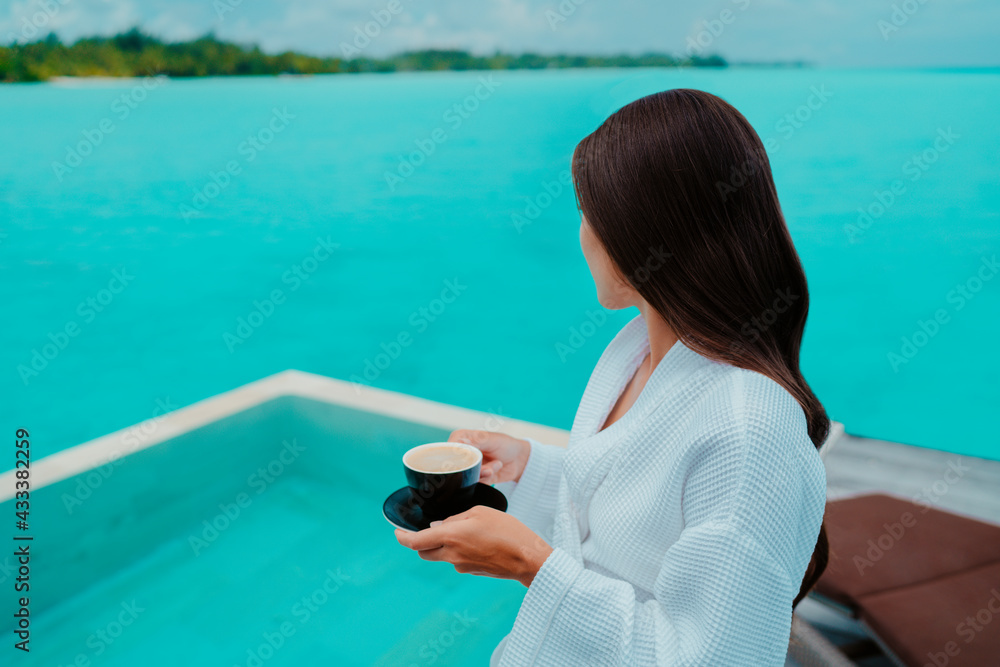 Woman having breakfast at luxury hotel room drinking coffee cup with view of turquoise ocean and overwater infinity swimming pool. Paradise getaway in the Maldives island. Woman having breakfast at luxury hotel room drinking coffee cup with view of turquoise ocean and overwater infinity swimming pool. Paradise getaway in the Maldives island.