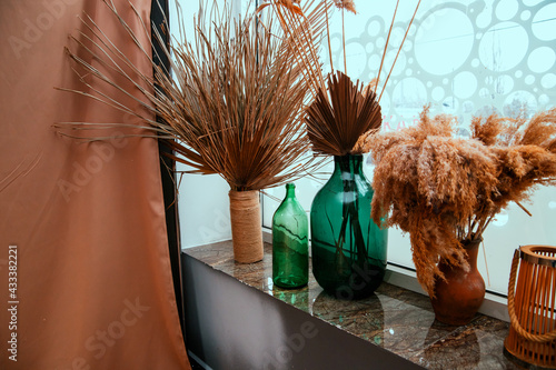 Dried palm leaves and reed branches in glass jars. Home decor stands on the windowsill.