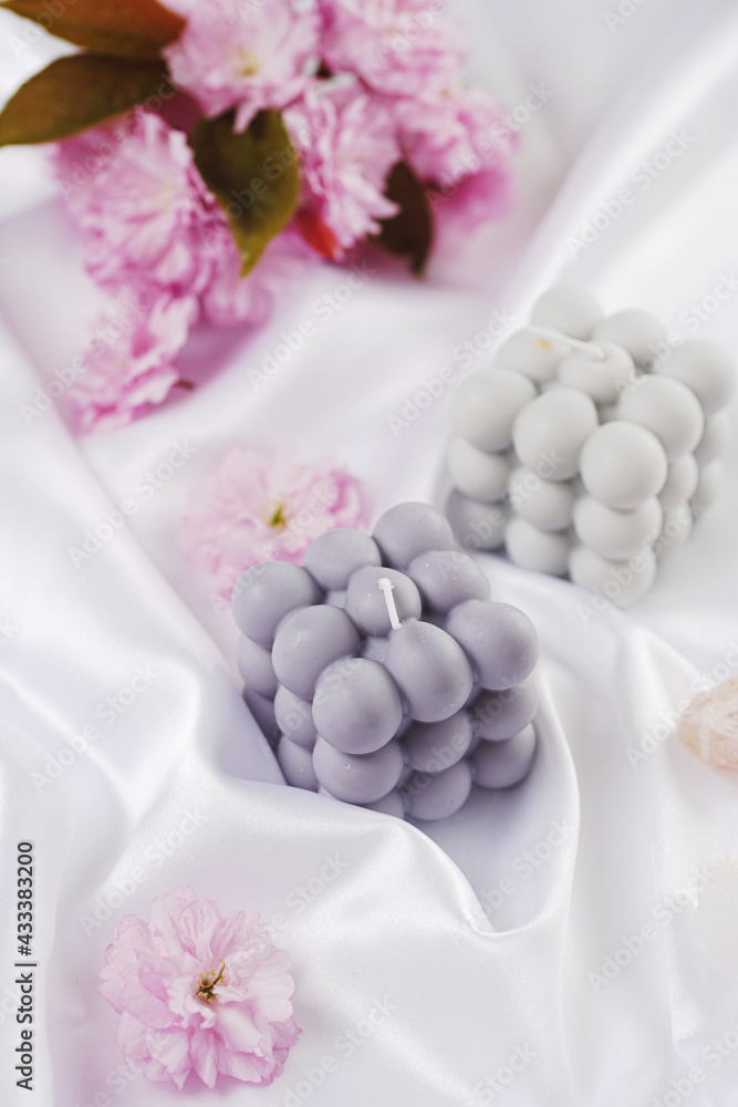 A grey-blue bubble candle on a white silky fabric and pink cherry blossom in the background