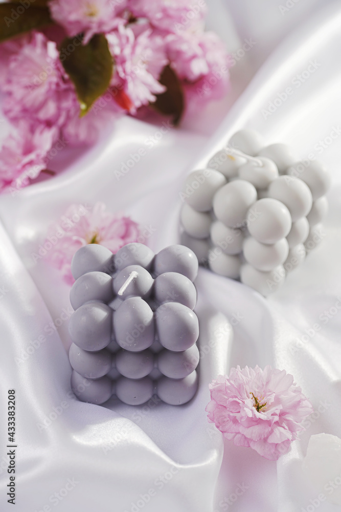 A grey-blue bubble candle on a white silky fabric and pink cherry blossom in the background A grey-blue bubble candle on a white silky fabric and pink cherry blossom in the background