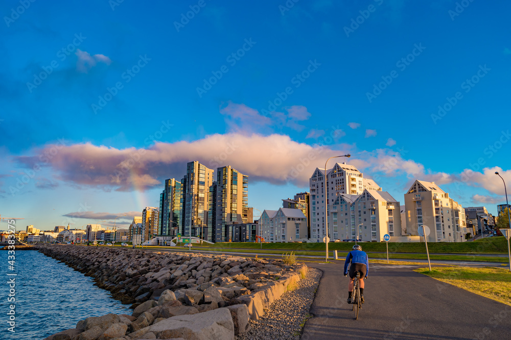 Cityscape over Reykjavik business and touristic downtown, embankment, ocean, harbor, modern buildings with cyclist at cycling lane at sunset skyline, Iceland, summer. - obrazy, fototapety, plakaty 