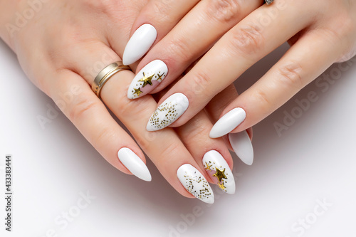Festive nail design. White manicure on sharp long nails close-up on a white background with painted gold stars. Gold casting on nails.