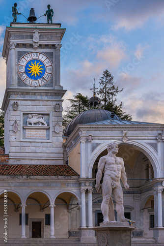 Hercules statue with clock tower in background. Italian classic art and architecture under a beautiful sky. Udine, Friuli Venezia Giulia, Italy.