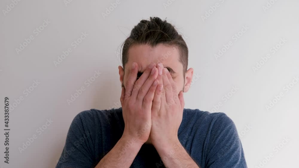 Young handsome Caucasian man coughs in palm of his hand and feels bad. Man is ill and coughing violently against white wall. Young handsome Caucasian man coughs in palm of his hand and feels bad. Man is ill and coughing violently against white wall.
