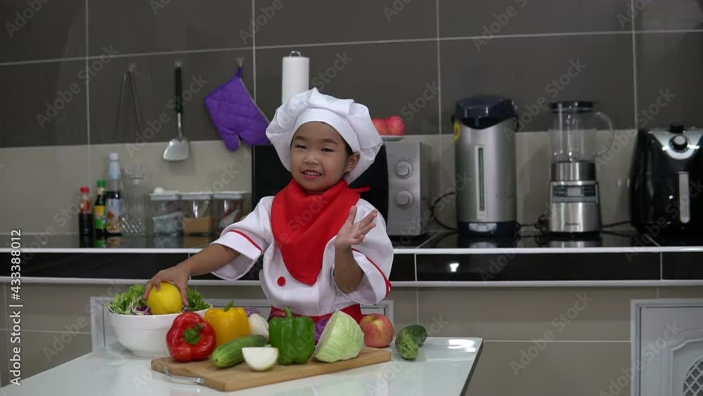 Cute asian girl wear chef uniform with a lot of vegatable on the table in the kitchen room,Make food for eat dinner,Funny time for kids Cute asian girl wear chef uniform with a lot of vegatable on the table in the kitchen room,Make food for eat dinner,Funny time for kids