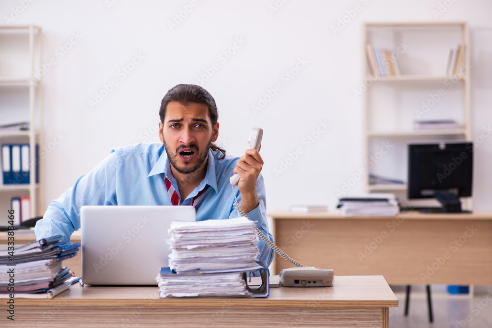 Young male employee unhappy with excessive work in the office Young male employee unhappy with excessive work in the office