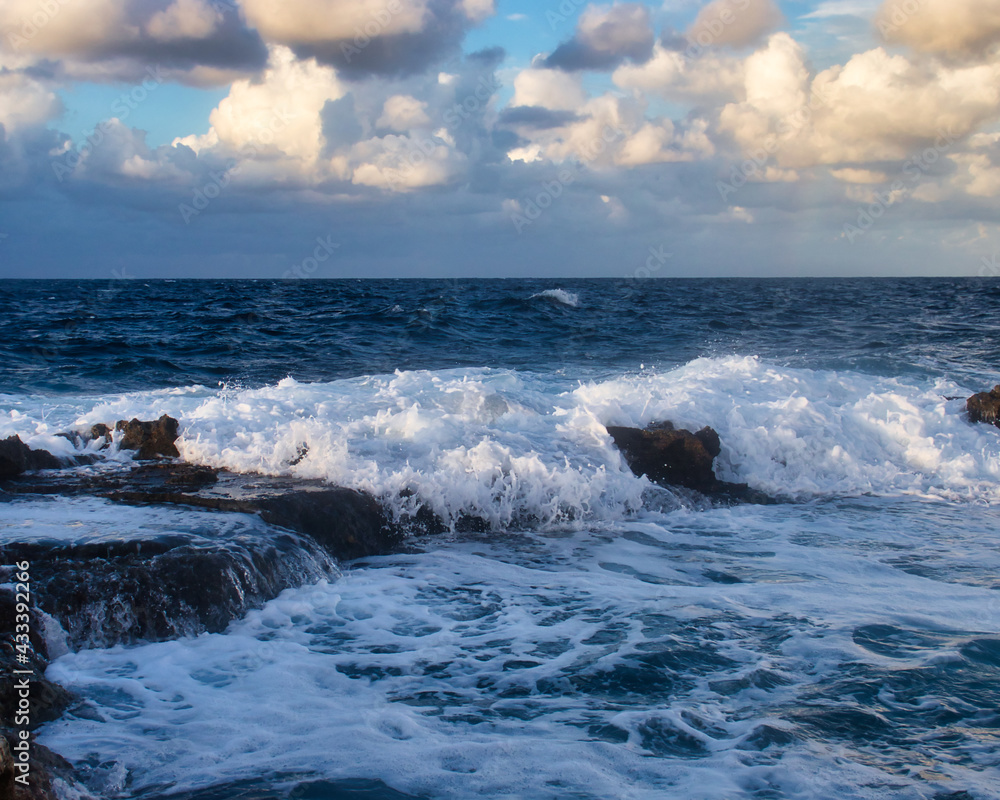 White water running over rocks in the blue ocean on a fall evening in Qawra, Malta.