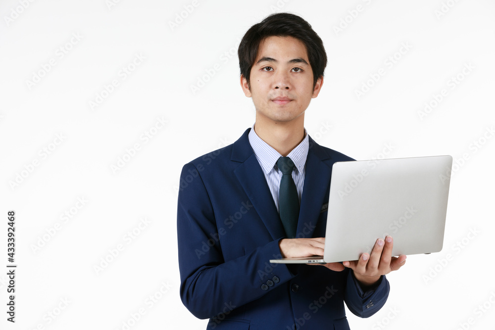 Young Asian businessman in a blue suit. Standing work in hand holding laptop. White background gives a formal feel, empty space can enter text. Young Asian businessman in a blue suit. Standing work in hand holding laptop. White background gives a formal feel, empty space can enter text.