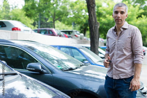 Adult man is holding key and standing near his modern car outdoor.