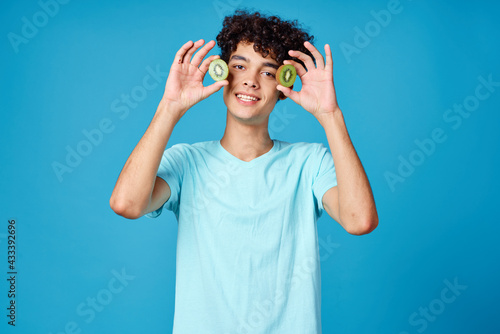 Cheerful guy with curly hair kiwi fruit blue background