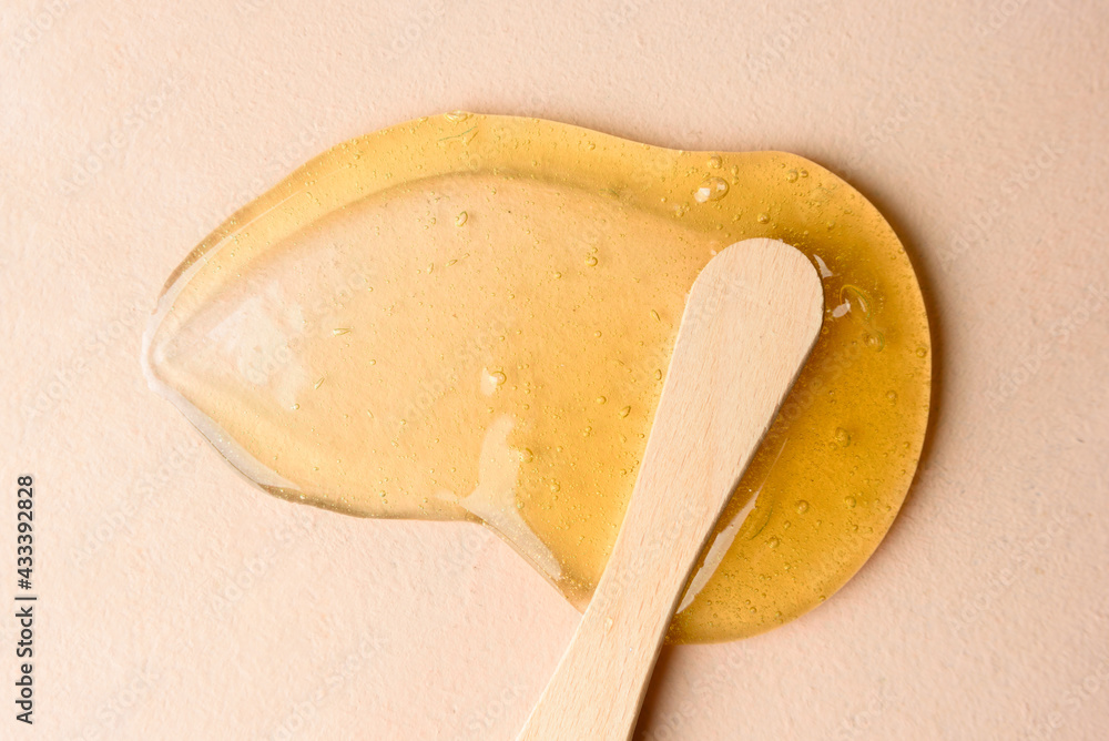 Liquid sugar wax smear with spatula on beige background - obrazy, fototapety, plakaty 