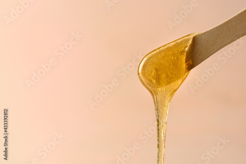 Liquid yellow sugar paste or wax for epilation on wooden stick or spatula closeup photo