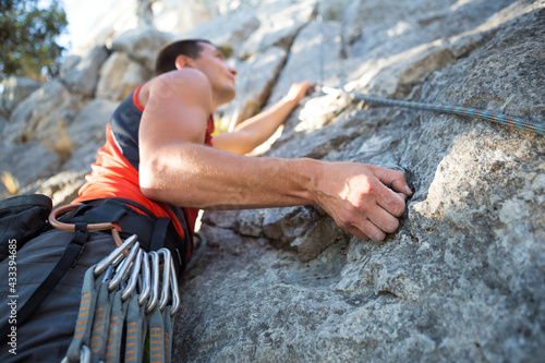 Climber in red t-shirt climbs a gray rock. A strong hand grabbed the lead, selective focus. Strength and endurance, climbing equipment: rope, harness, chalk, chalk bag, carabiners, braces, quickdraws