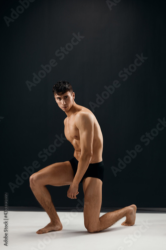 man in black shorts kneels on a dark background