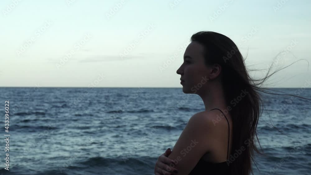 A young brunette woman with long hair walks along the beach. Woman looking at the horizon at night. 4k footage A young brunette woman with long hair walks along the beach. Woman looking at the horizon at night. 4k footage