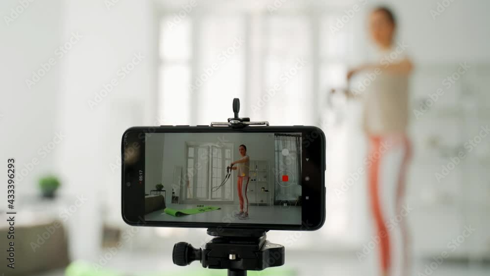 The girl shoots her fitness video blog on a smartphone. The girl conducts distance fitness training online. The girl shoots a video blog during fitness. Physical exercises. The girl shoots her fitness video blog on a smartphone. The girl conducts distance fitness training online. The girl shoots a video blog during fitness. Physical exercises.