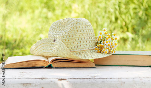 Fototapeta Naklejka Na Ścianę i Meble -  Chamomile flowers, book and summer hat in sunny garden. relax time, summer season concept. Rustic composition