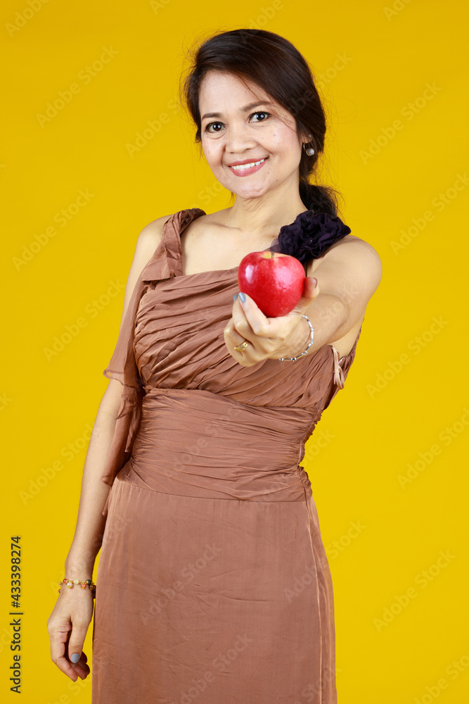 Senior cute Asian woman holding and showing apple, studio shot on yellow background. Senior cute Asian woman holding and showing apple, studio shot on yellow background.