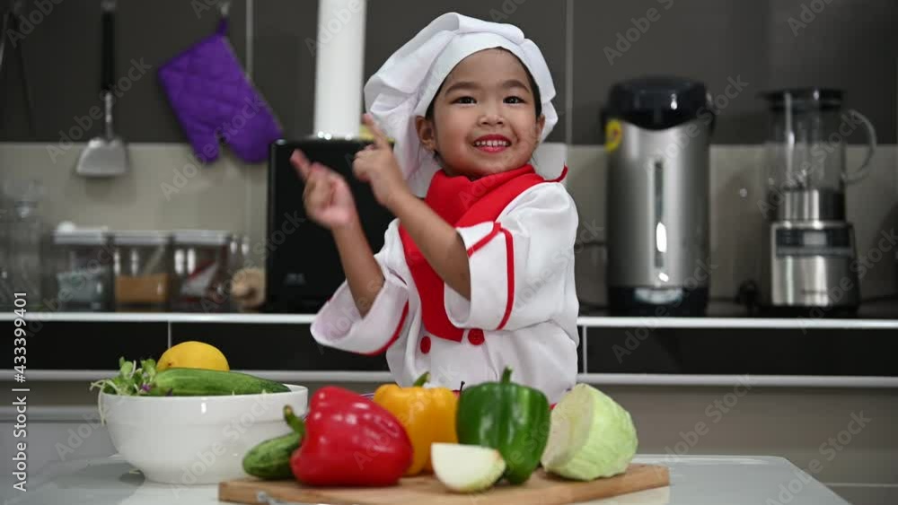 Cute asian girl wear chef uniform with a lot of vegatable on the table in the kitchen room,Make food for eat dinner,Funny time for kids