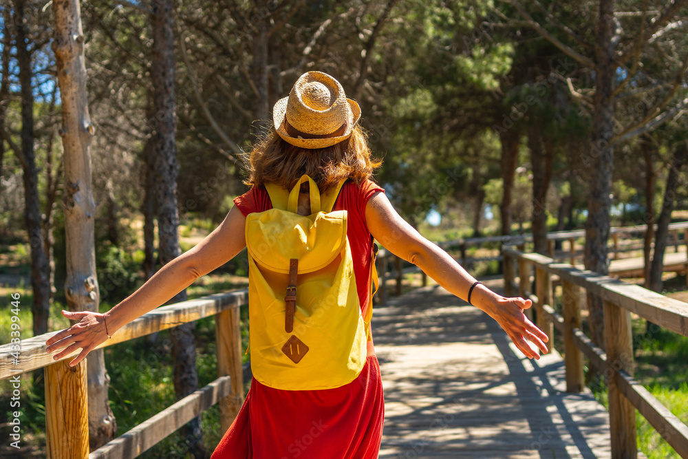 A young woman in a red dress walking along the wooden walkway towards Moncayo Beach in Guardamar del Segura, Alicante. Community of Valencia. Spain