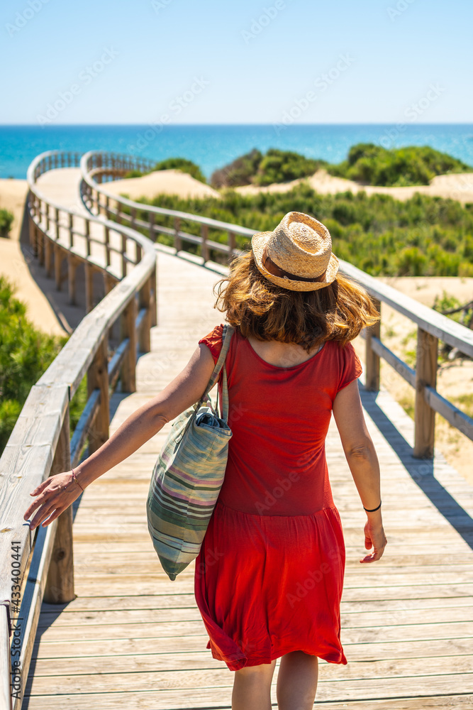 Girl with red dress on the wooden path to Playa Moncayo in Guardamar del Segura next to Torrevieja, Alicante. Community of Valencia. Spain, holidays in the Mediterranean