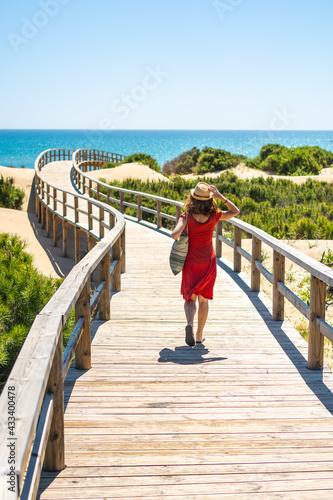 Girl with red dress on the wooden path to Playa Moncayo in Guardamar del Segura next to Torrevieja, Alicante. Community of Valencia. Spain, holidays in the Mediterranean