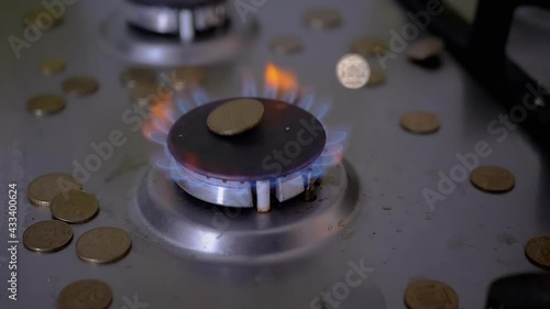 Gas burner with a scattering of coins on the stove. Coins fall on the Gas burner, which glowing with a blue flame in the kitchen. Gas price increase. Save natural gas resources. Slow motion. 180 fps. photo