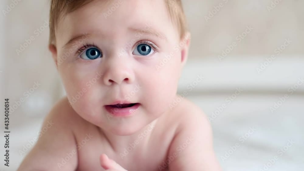 Close up portrait of smiling lovely little baby boy. Beautiful infant kid is lying on the white bed on his stomach. A nice little caucasian newborn baby. Close up portrait of smiling lovely little baby boy. Beautiful infant kid is lying on the white bed on his stomach. A nice little caucasian newborn baby.