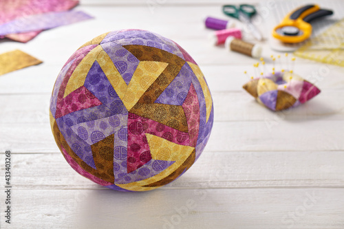 Patchwork ball made of pieces of fabric sewn in the shape of the letter Z on the background of quilting and sewing accessories
