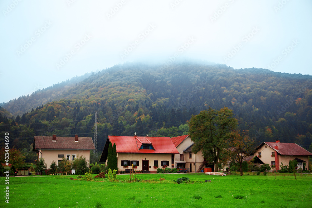 Idyllic mountain village landscape with little houses with red roof and vast green lawns. Evening dusk time, after sunset, beautiful nature, blue mist on the hills. Outdoors, copy space.