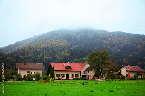 Idyllic mountain village landscape with little houses with red roof and vast green lawns. Evening dusk time, after sunset, beautiful nature, blue mist on the hills. Outdoors, copy space.