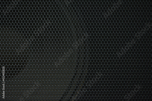 Close-up of a dark speaker grille with a speaker in the background