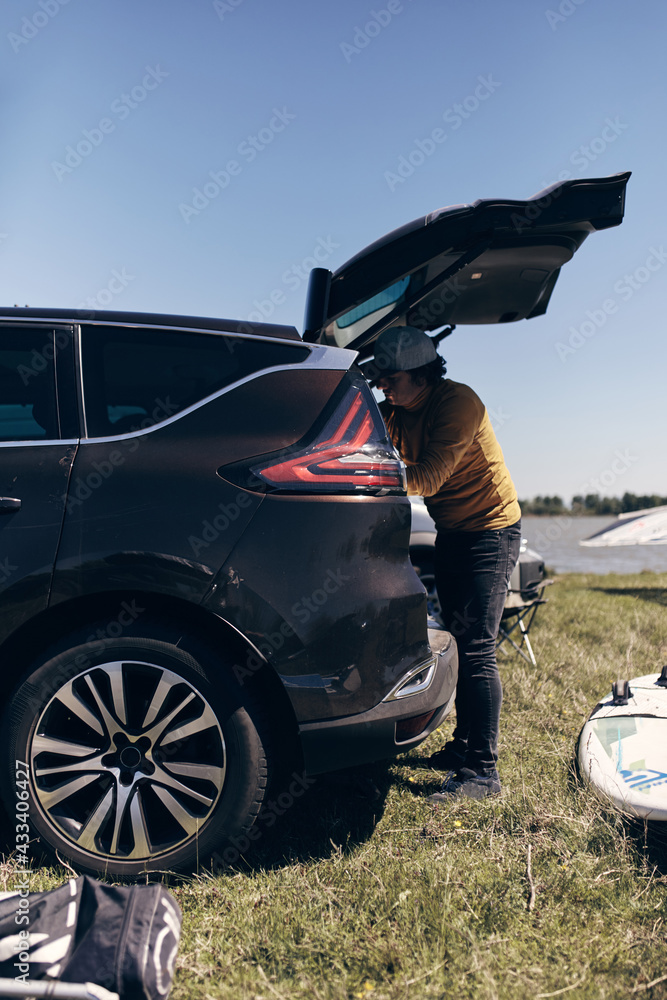 Windsurfer and camper packing and unpacking from a car's roof rack in nature. Windsurfer and camper packing and unpacking from a car's roof rack in nature.