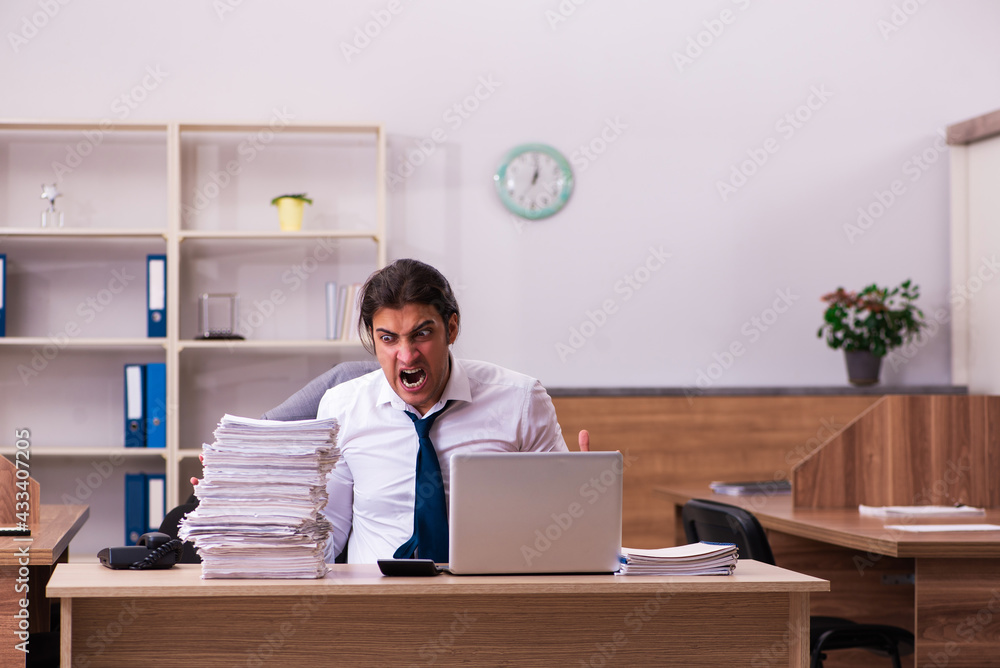 Young male employee unhappy with excessive work in the office Young male employee unhappy with excessive work in the office