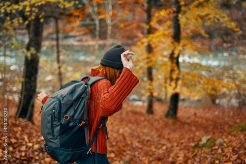 woman in a sweater with a backpack resting in a park near the river in nature in autumn