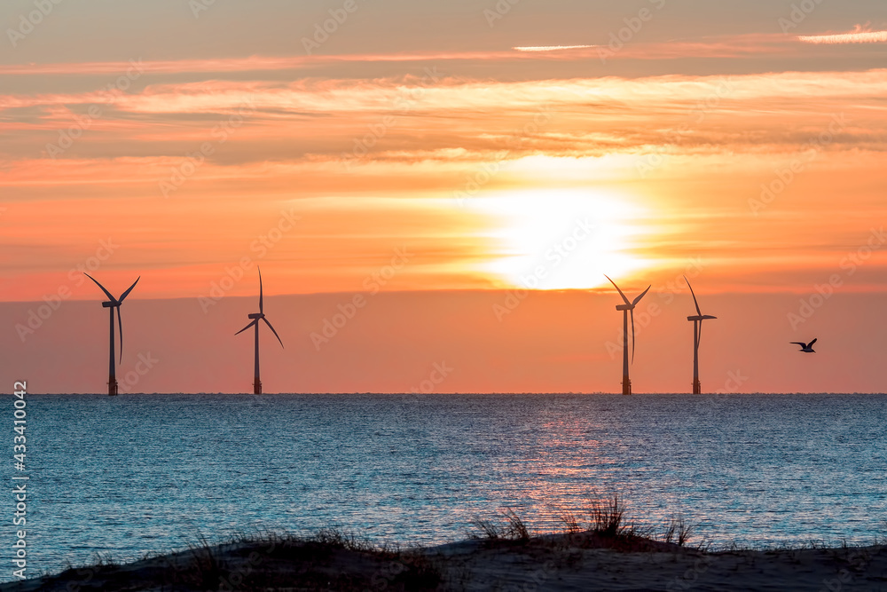 Obraz premium Tropical island sunset with offshore wind farm turbines on ocean horizon. Beautiful sunrise over the sea