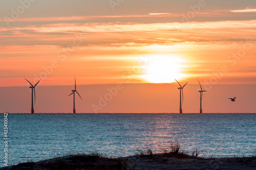 Tropical island sunset with offshore wind farm turbines on ocean horizon. Beautiful sunrise over the sea