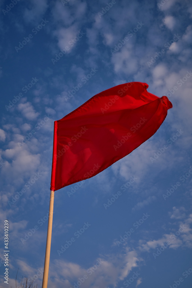 Red flag with blue sky with clouds, strong wind flying red flag. Red