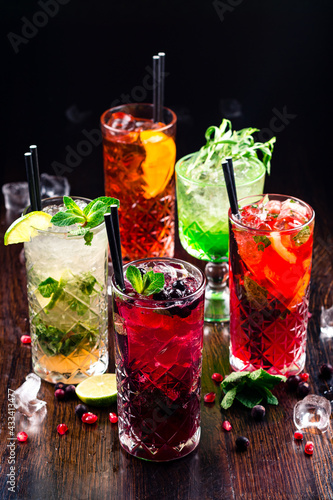 Selection of gin tonic with blackberries, with orange, with lime and mint leaves. In glasses on a rustic wooden background