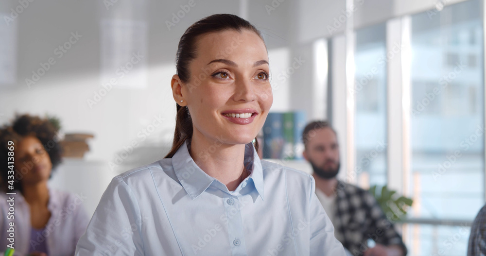 Portrait of smiling young woman student in class listening to teacher and taking notes Portrait of smiling young woman student in class listening to teacher and taking notes