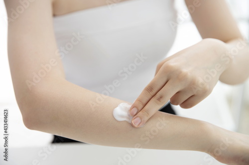 Young woman applying moisturizer on arm
