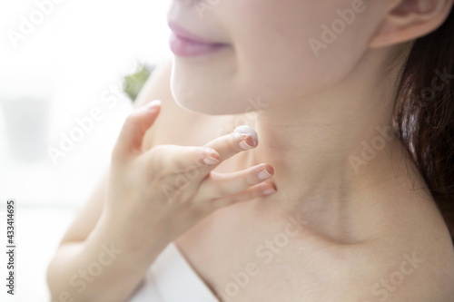 Young woman applying moisturizer on neck