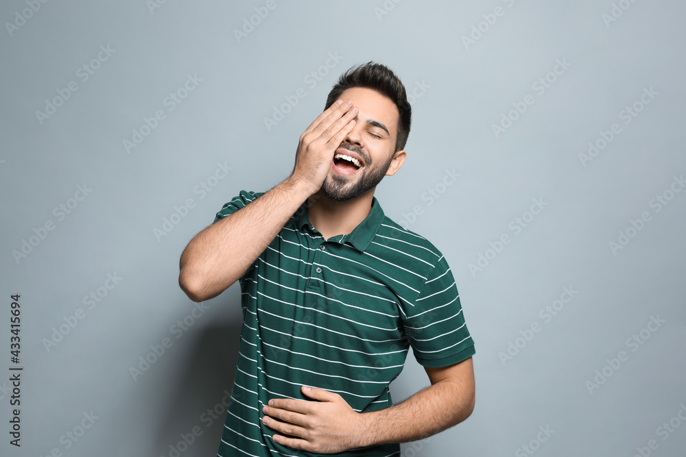 Young man laughing on light grey background. Funny joke Young man laughing on light grey background. Funny joke