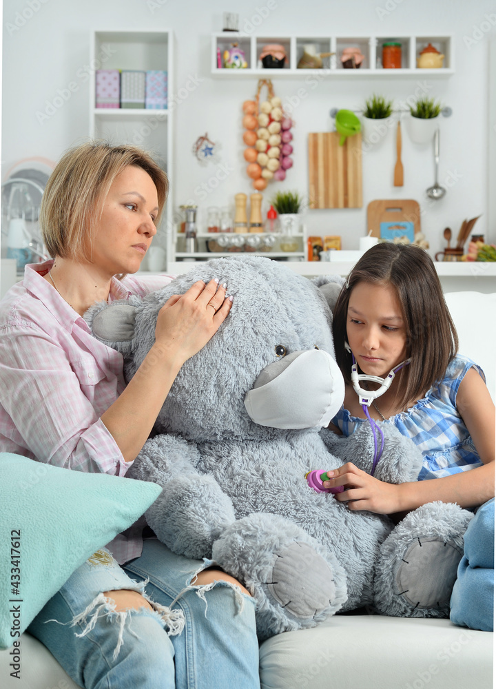  little girl and mother playing   with toy bear in facial mask. Girl with stethoscope