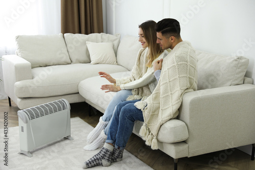 Happy couple sitting on sofa near electric heater at home