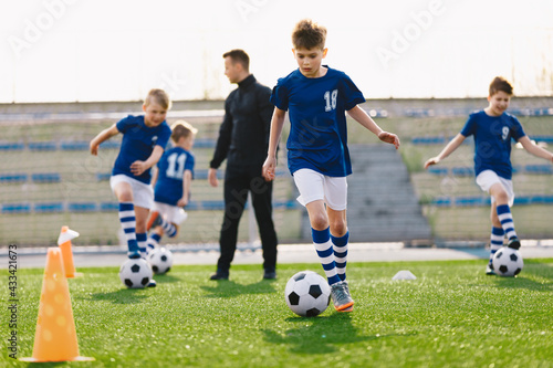 School Kids Play Team Sports on Soccer Stadium. Happy Boys Kicking Football Balls on Grass Field. Young Coach Coaching Children in the Background