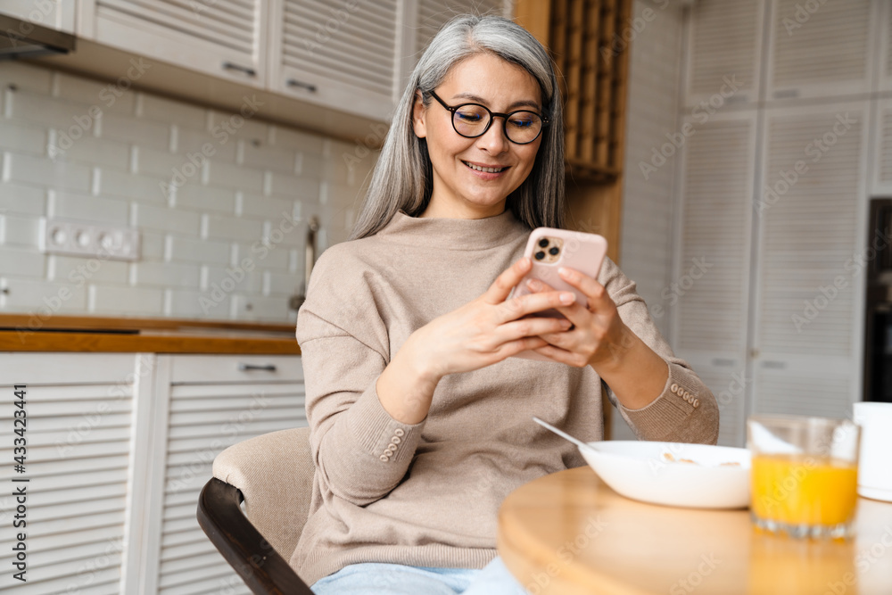 Mature smiling woman using cellphone while having breakfast Mature smiling woman using cellphone while having breakfast